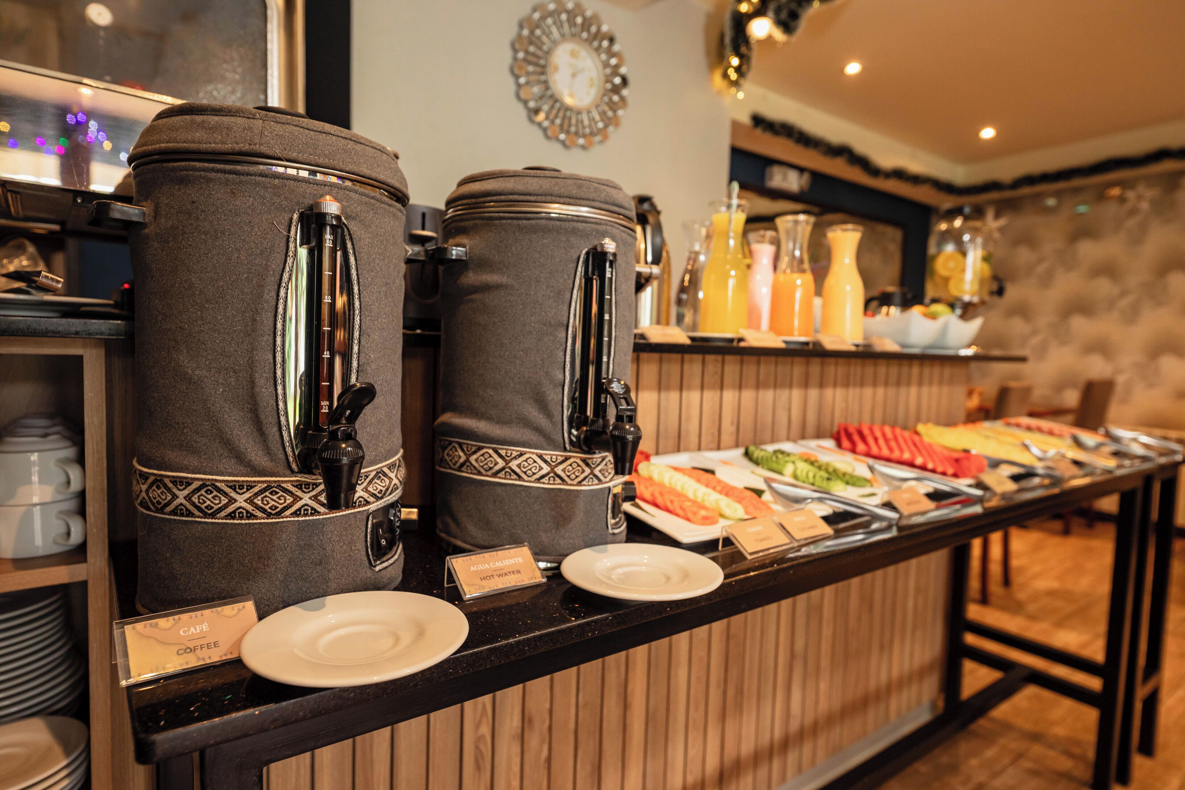 A buffet setup with coffee and hot water dispensers, a variety of food items, and a clock on the wall.