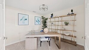 Quarto moderno e bem iluminado, com escrivaninha de madeira, duas pinturas abstratas emolduradas, uma planta em vaso e uma estante de ferro em formato de escada.