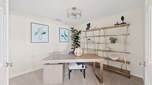 A modern, well-lit room with a wooden desk, two framed abstract paintings, a potted plant, and a metal ladder shelf. - Coastal Condo with Resort Style Amenities Including Golf (Punta Gorda)