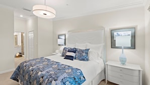 Quarto com cama grande, mesa de cabeceira, luminária na parede e quadro emoldurado.