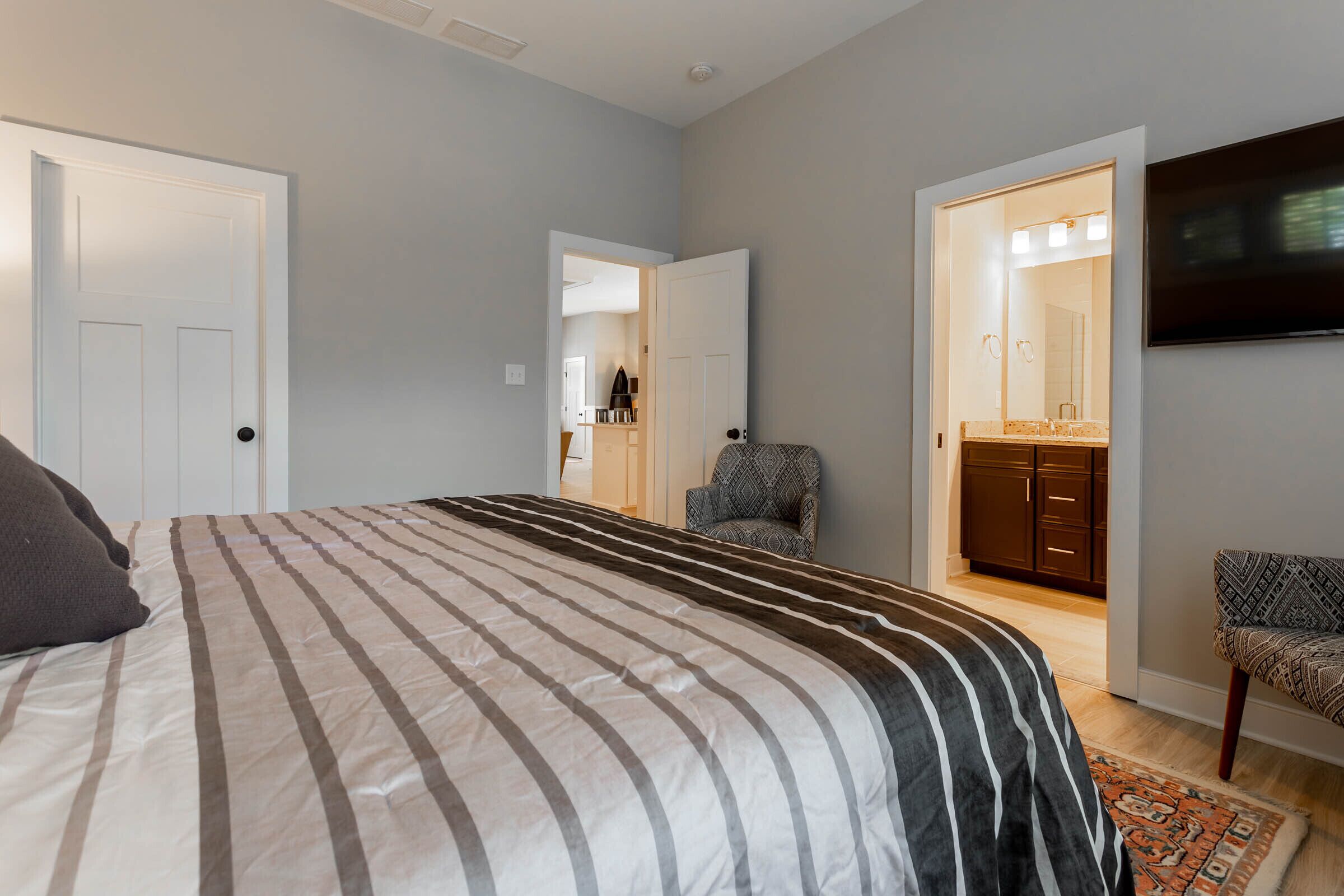A bedroom with a large bed, a TV mounted on the wall, and a bathroom visible through an open door.