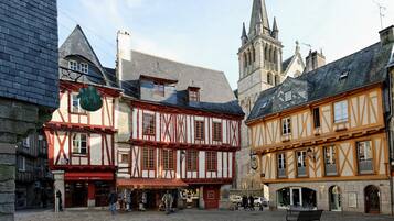 Une rue pavée bordée de bâtiments traditionnels à colombages, avec un clocher d’église et un banc.