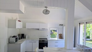 A modern kitchen with white cabinetry, a dining table, and a window with a view of greenery.