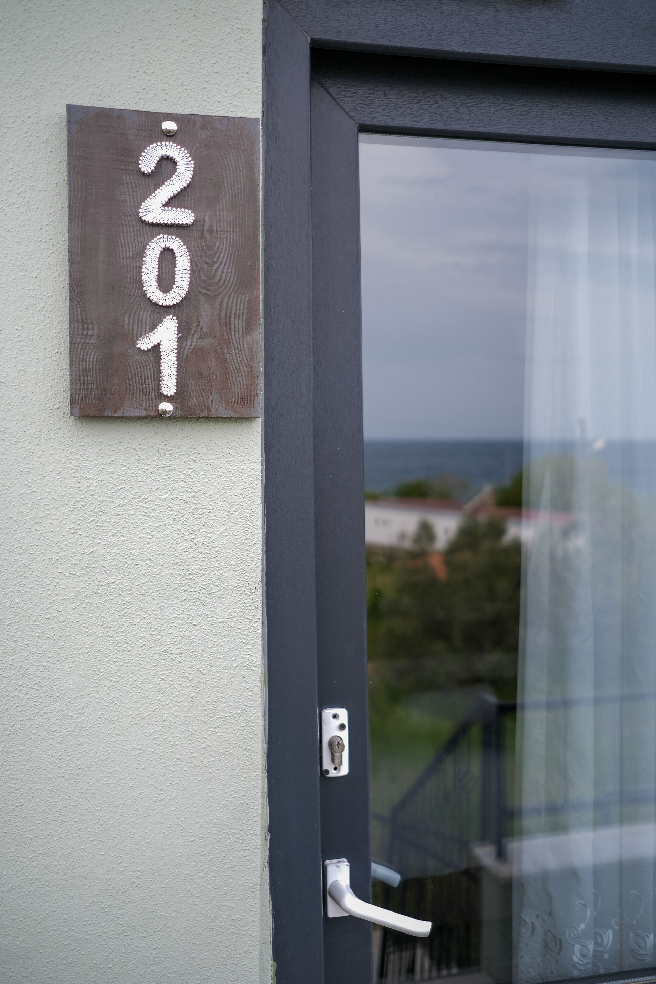 Una puerta con una placa que indica el número '201' y vista al mar a través de una puerta de vidrio.