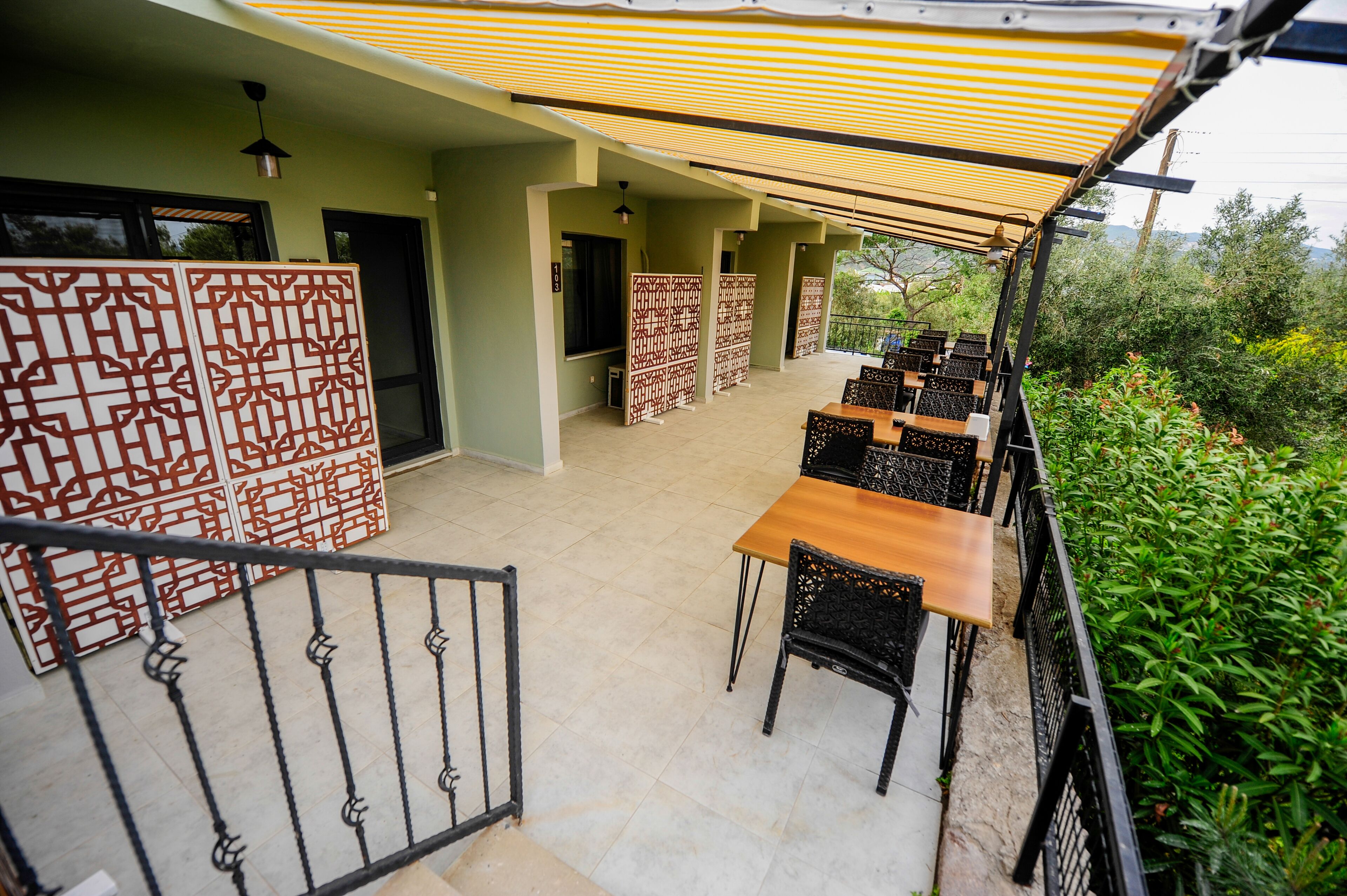 Un patio al aire libre con mesas y sillas, un área de estar cubierta y paneles decorativos.