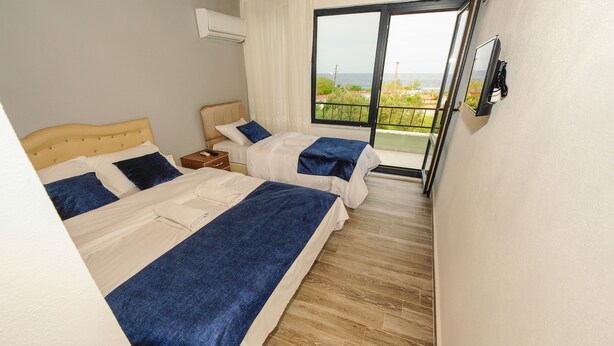 A hotel room with two beds, a TV mounted on the wall, and a balcony with a view of the sea. - Assos No9 Hotel (Ayvacik)