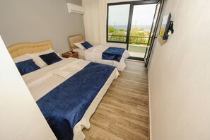 Een hotelkamer met twee bedden, een aan de muur bevestigde televisie, en een balkon met uitzicht op zee.