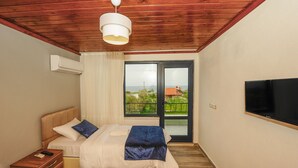 A bedroom with a bed, a bedside table, a TV mounted on the wall, and a window with a view of the outside. - Assos No9 Hotel (Ayvacik)