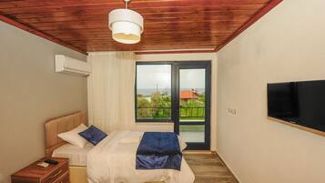 A bedroom with a bed, a bedside table, a TV mounted on the wall, and a window with a view of the outside.