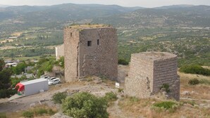 A historical stone structure with a tower and a cylindrical building, surrounded by a hilly landscape. - Assos No9 Hotel (Ayvacik)