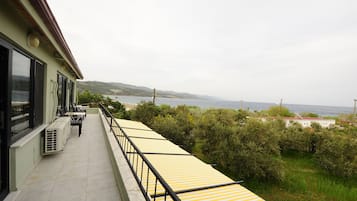 Un balcón con toldos a rayas amarillas, unidades de aire acondicionado y vistas al mar y las colinas.