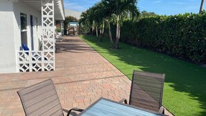A patio with brick flooring, two wicker chairs, and a table.