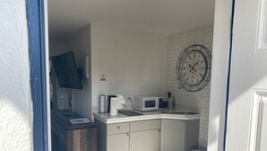 Een kleine keuken met een magnetron, broodrooster en een klok aan de muur.