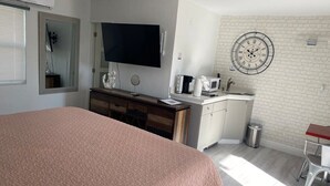 Een slaapkamer met een groot bed, een televisie, een bureau en een keukenhoek met een magnetron.