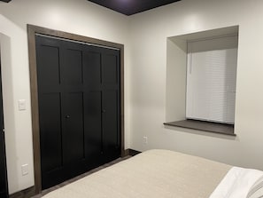 Ein Schlafzimmer mit einem Bett, einem dunklen Holzschrank, einem Fenster mit Jalousien und einem Lichtschalter an der Wand.