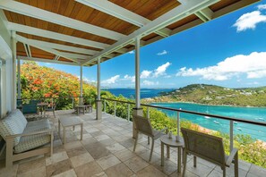 A covered outdoor seating area with a view of the ocean and hills. - Luxury Villa | Ocean & Sunset Views | by BookVI (Cruz Bay)