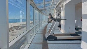 A modern, sunlit corridor with large windows offering views of the beach and ocean.
