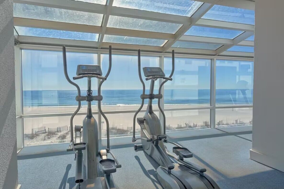 A gym with two elliptical machines and a large window overlooking a beach.