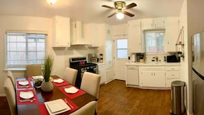 A compact kitchen with white cabinets, a stove, and a microwave. There is a dining table set with red placemats and white plates. - Bright 2 Bedroom Cozy HOUSE! Pasadena/Alhambra Prime Location! Dogs OK! (Alhambra)