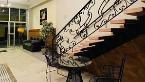 En modern entréhall med en trappa, en sittgrupp med bord och stolar samt ett mönstrat golv.