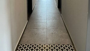 En smal, väl upplyst hall med ett klinkergolv och utsikt över en balkong med grönska.