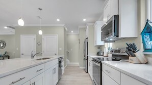 A modern kitchen with white cabinetry, stainless steel appliances, and a central island. - New Townhome with Private Beach Club (Pensacola)