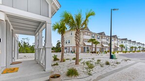 A beachfront property with a covered porch, palm trees, and a row of townhouses. - New Townhome with Private Beach Club (Pensacola)