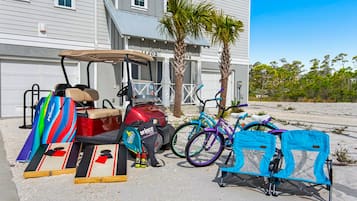 Un carrito de golf, bicicletas y una tienda de campaña montadas sobre una zona arenosa frente a una casa con garaje.
