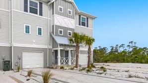 A two-story house with a garage, a covered porch, and a sandy driveway. - New Townhome with Private Beach Club (Pensacola)