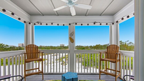 A covered porch with two wooden Adirondack chairs, a ceiling fan, and a view of the beach. - New Townhome with Private Beach Club (Pensacola)