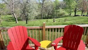 A wooden deck with red Adirondack chairs and a yellow table. - Tranquil Home in Beautiful Setting (Ames)