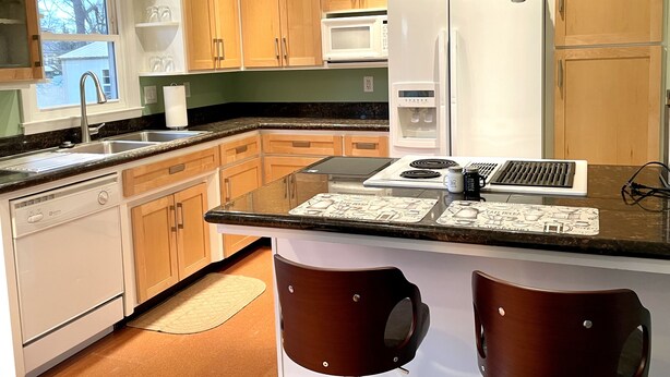 A modern kitchen with wooden cabinets, a stainless steel sink, a built-in microwave, a white refrigerator, and a coffee maker on the counter. - Tranquil Home in Beautiful Setting (Ames)