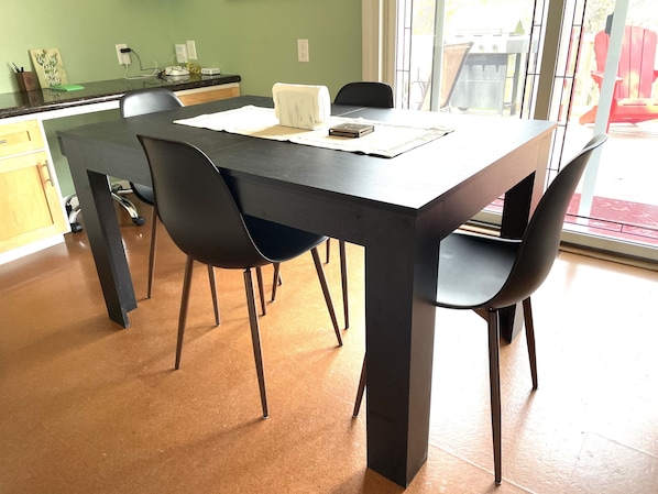A dining area with a black table, four chairs, and a window with a view of the outside. - Tranquil Home in Beautiful Setting (Ames)