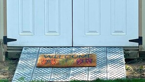 A double door with a sign above reading "HOT TUB DR" and a welcome mat with colorful designs at the entrance. - Tranquil Home in Beautiful Setting (Ames)