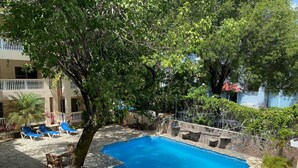 Una piscina con baldosas de piedra, rodeada de sillones de descanso y un árbol.