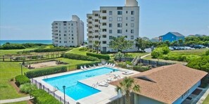 A resort with a swimming pool, multiple-story buildings, and a view of the ocean.