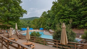 A wooden deck with picnic tables and umbrellas overlooking a swimming pool area surrounded by trees. - Lake's Edge Lodge - Water Views, & Community Golf! (Big Canoe)