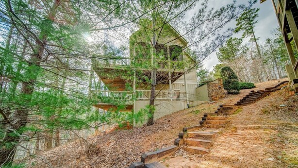 A multi-level wooden structure with a staircase leading up to it, surrounded by trees and a dry grassy area. - Lake's Edge Lodge - Water Views, & Community Golf! (Big Canoe)