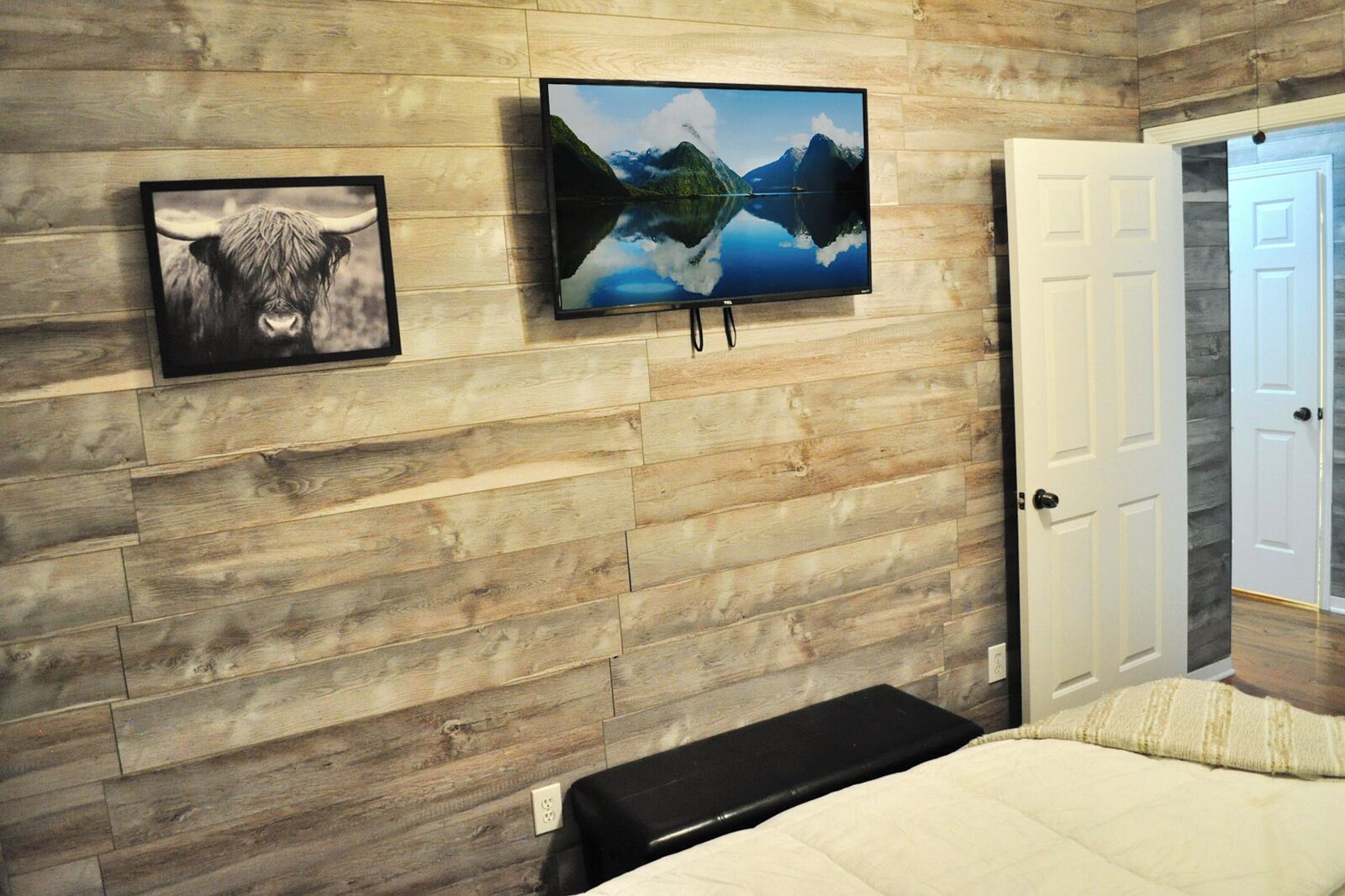 A bedroom with a wooden wall, a bed, a TV, and a door.