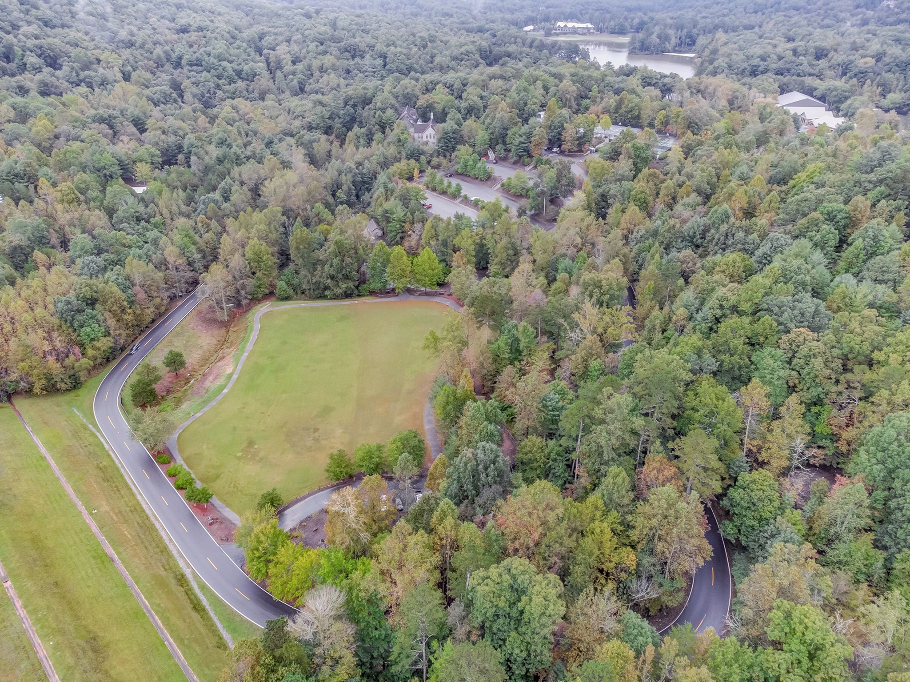 An aerial view of a residential area with a winding road, a large open field, and dense forest.