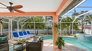 A covered outdoor area with a pool, lounge chairs, and a ceiling fan.