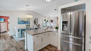 A modern kitchen with white cabinetry, a large stainless steel refrigerator, and a dining area with a white table and chairs.