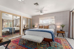 A bedroom with a large bed, a mirror, a ceiling fan, and a colorful rug. - Tortoise Oasis - Hot tub, Shuffleboard, & More! (Yucca Valley)