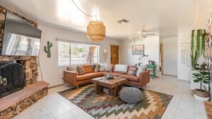 A living room with a stone fireplace, a large sectional sofa, a coffee table, and a hanging rattan light fixture.