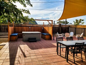 A patio with a hot tub, outdoor seating, and a wooden fence. - Tortoise Oasis - Hot tub, Shuffleboard, & More! (Yucca Valley)