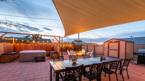 An outdoor patio with a wooden table and chairs, a hot tub, and a barbecue grill.