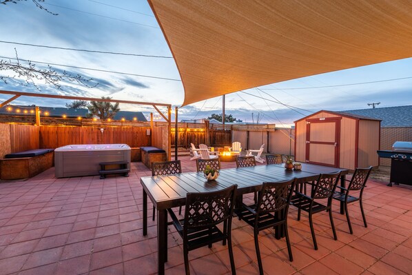 An outdoor patio with a wooden table and chairs, a hot tub, and a barbecue grill. - Tortoise Oasis - Hot tub, Shuffleboard, & More! (Yucca Valley)