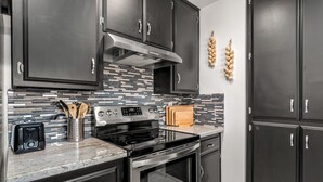 A modern kitchen with dark cabinets, a stainless steel range hood, a granite countertop, and a tiled backsplash.