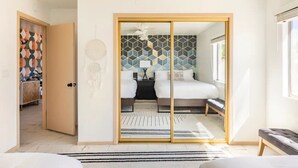 A modern bedroom with a large sliding door leading to a bathroom, a bed with a geometric-patterned headboard, and a bedside table with a lamp.