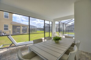 A patio area with a table and chairs, large windows, and a view of a residential neighborhood. - Private Pool, Spa and Premium Resort Amenities Included! (Kissimmee)